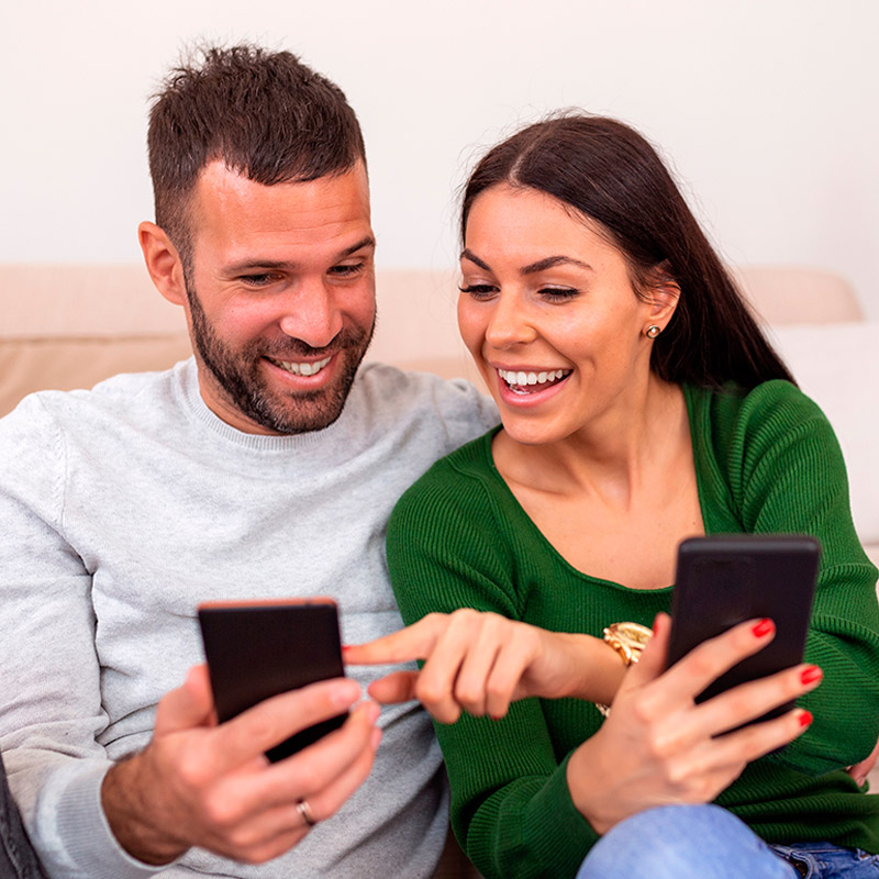 Hombre y mujer sonriendo, cada uno sosteniendo un celular Hombre y mujer sonriendo, cada uno sosteniendo un celular