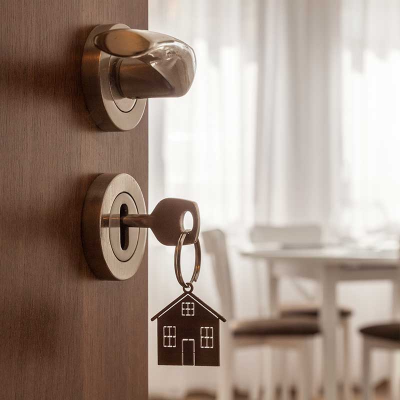 Puerta de una vivienda con llaves puestas en chapa, al fondo se ve mesa con sillas