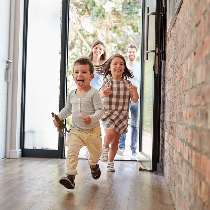 Dos niños pequeños entran corriendo a su casa, atrá de ellos vienen sus padres