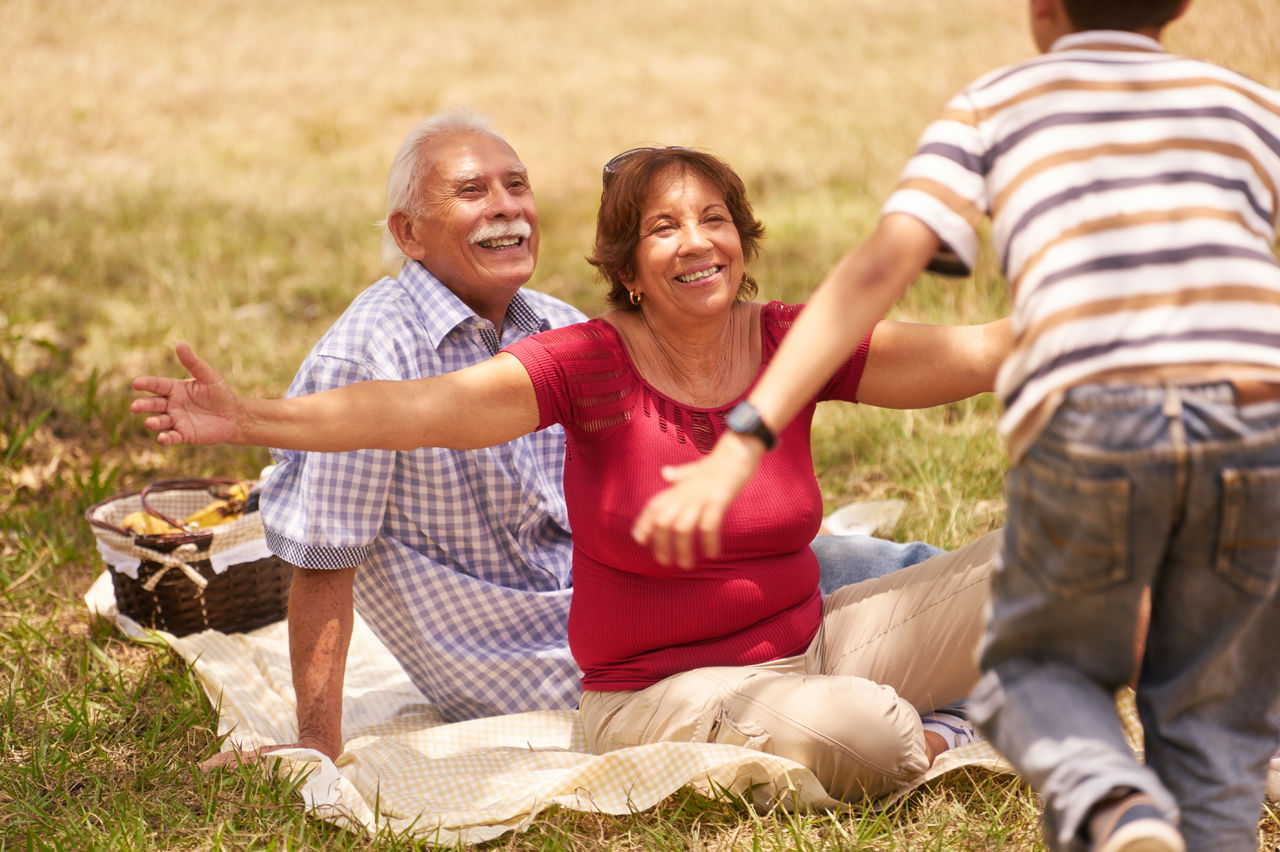 Pareja de adulto mayor sentados al aire libre. Abuela con brazos abiertos a punto de abrazar a un niño 