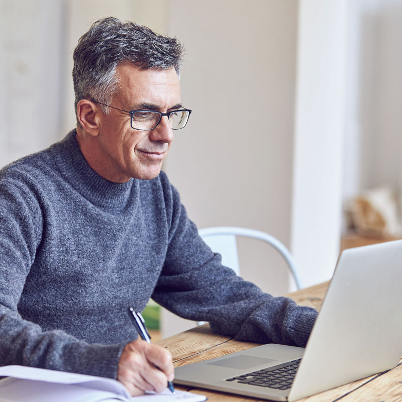 Hombre trabajando en su computador y escribiendo en una libreta